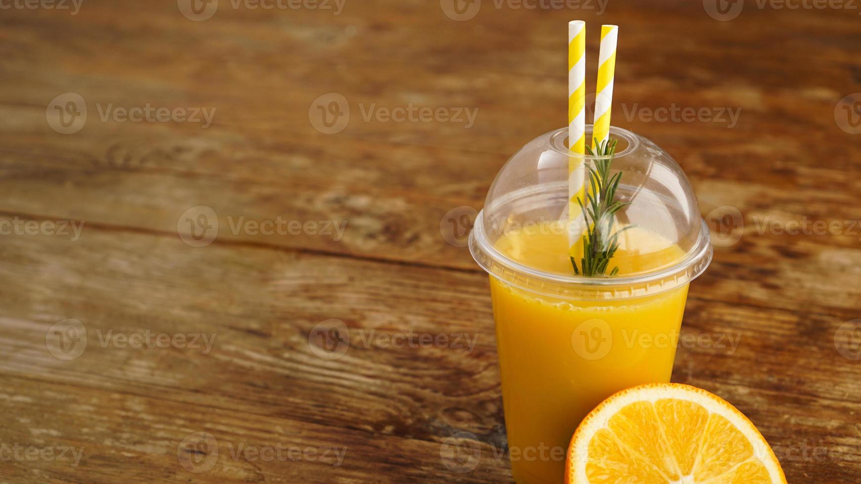 Jugo de naranja en comida rápida taza cerrada con tubos sobre mesa de madera foto