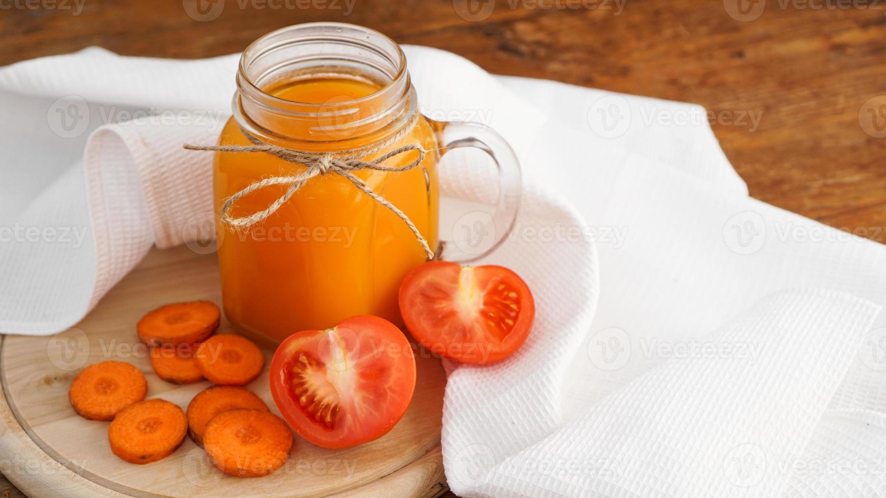 Fresh carrot and tomato juice in glass on wooden table photo