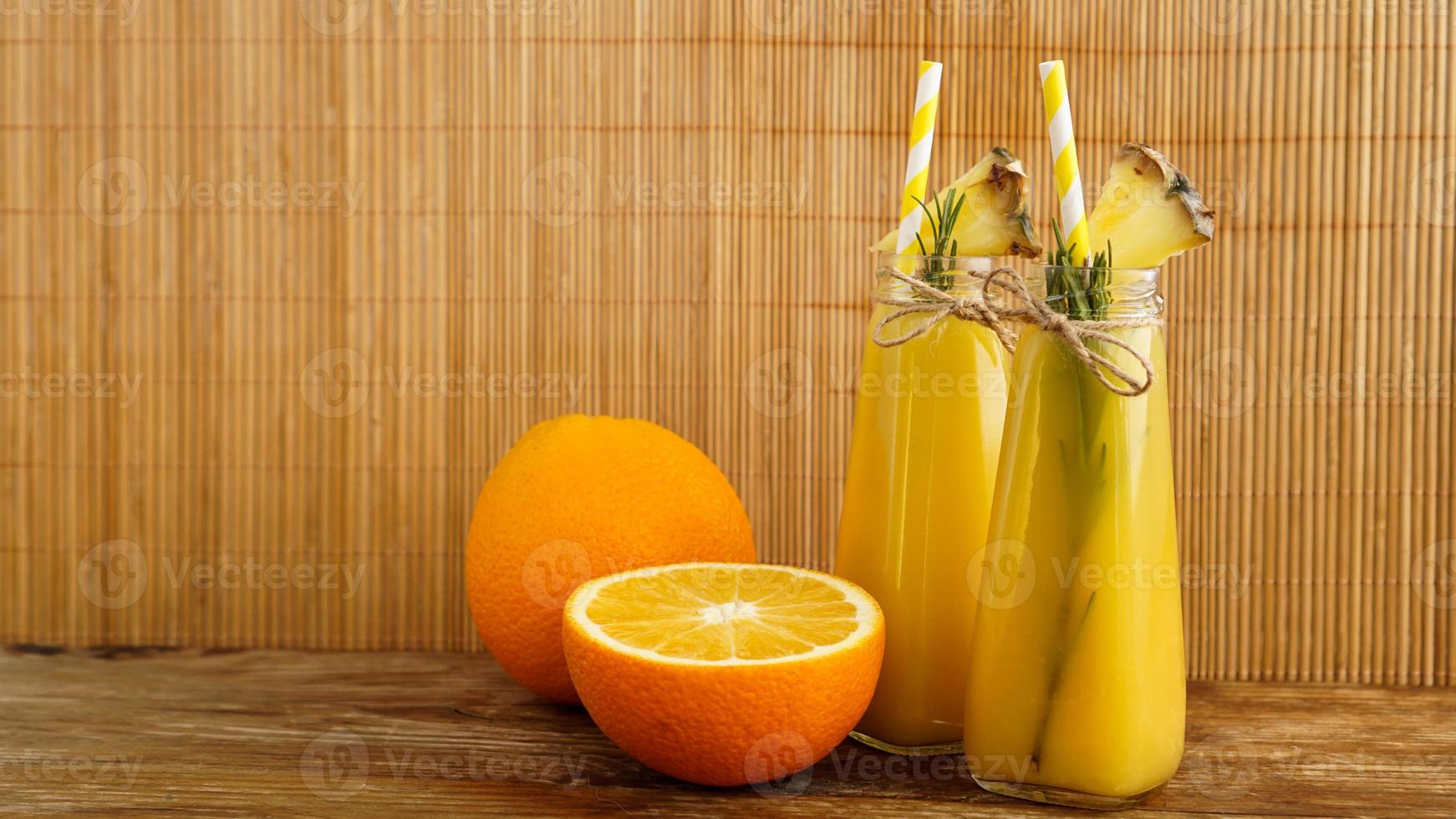 Two bottles of tropical juice with paper straws. Oranges and pineapple photo