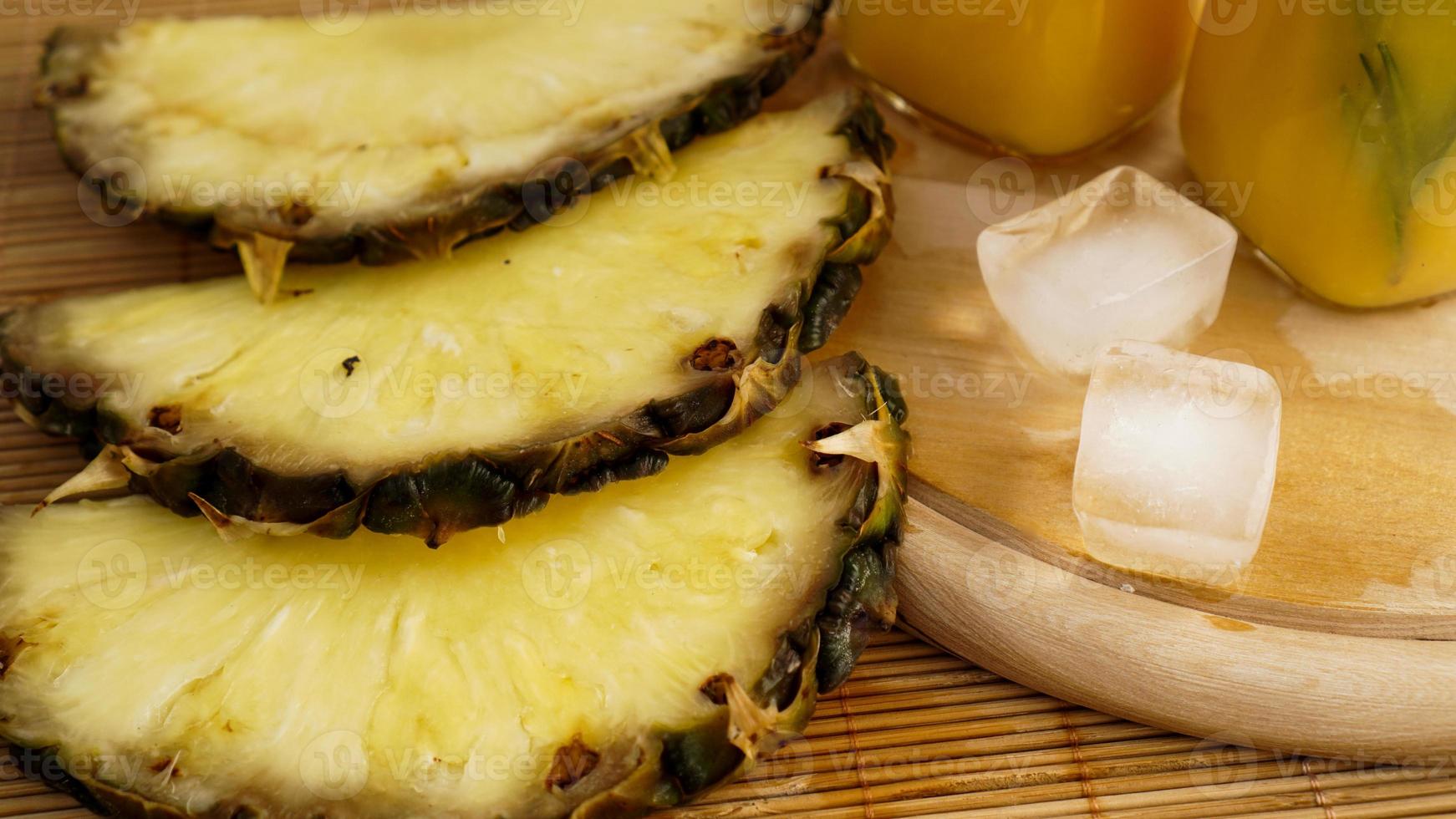 Fresh pineapple slices and and ice cubes on a wooden background photo