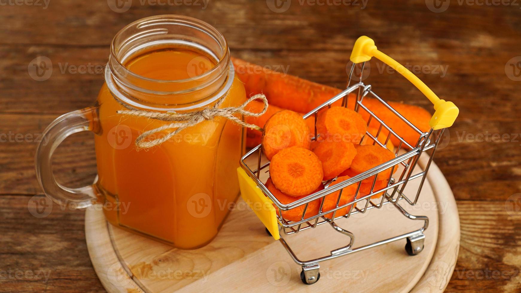 Jugo de zanahoria fresca con carrito de supermercado y sobre fondo de madera foto