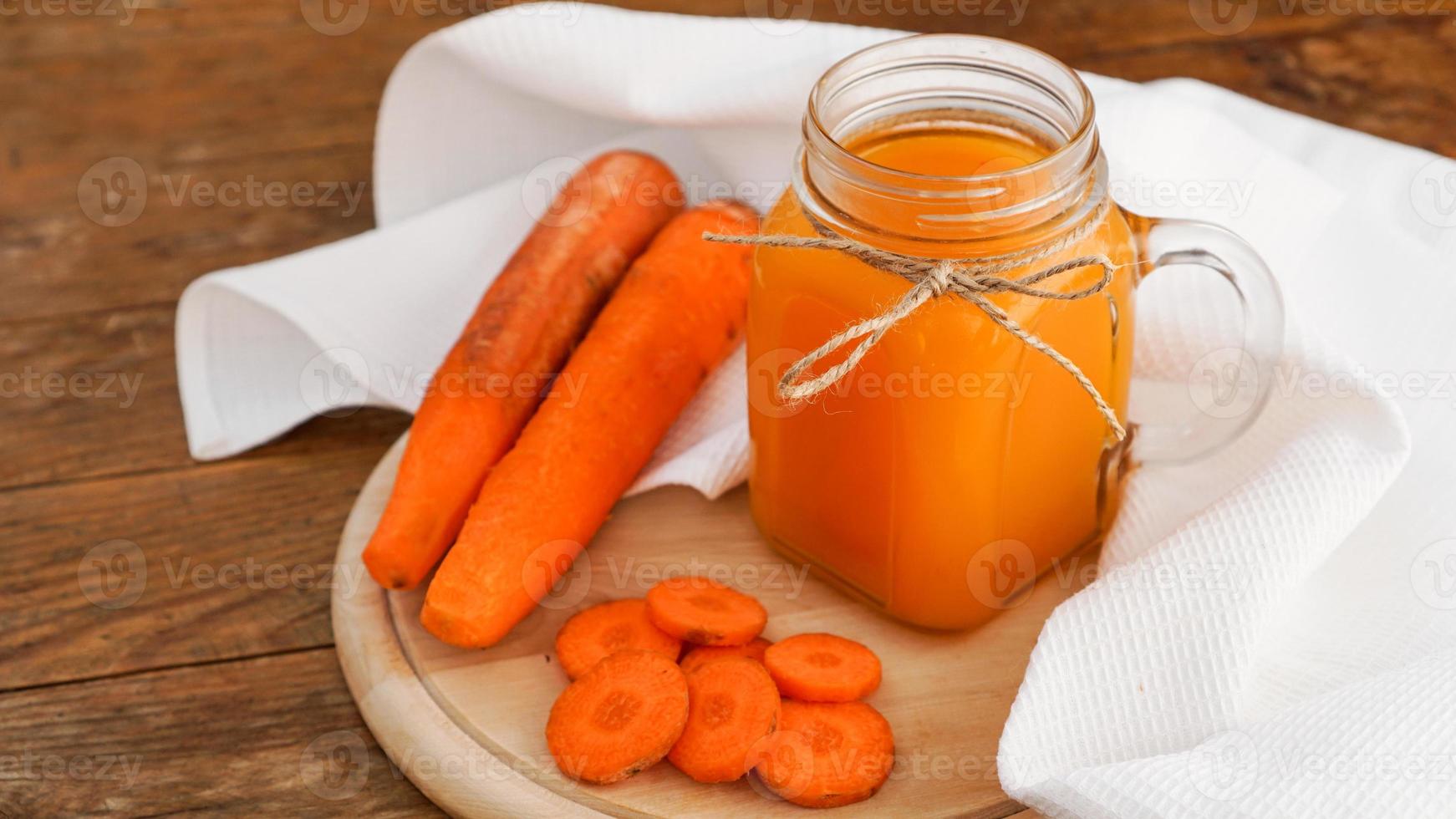 Jugo de zanahoria naranja brillante en un frasco de vidrio sobre un fondo de madera foto