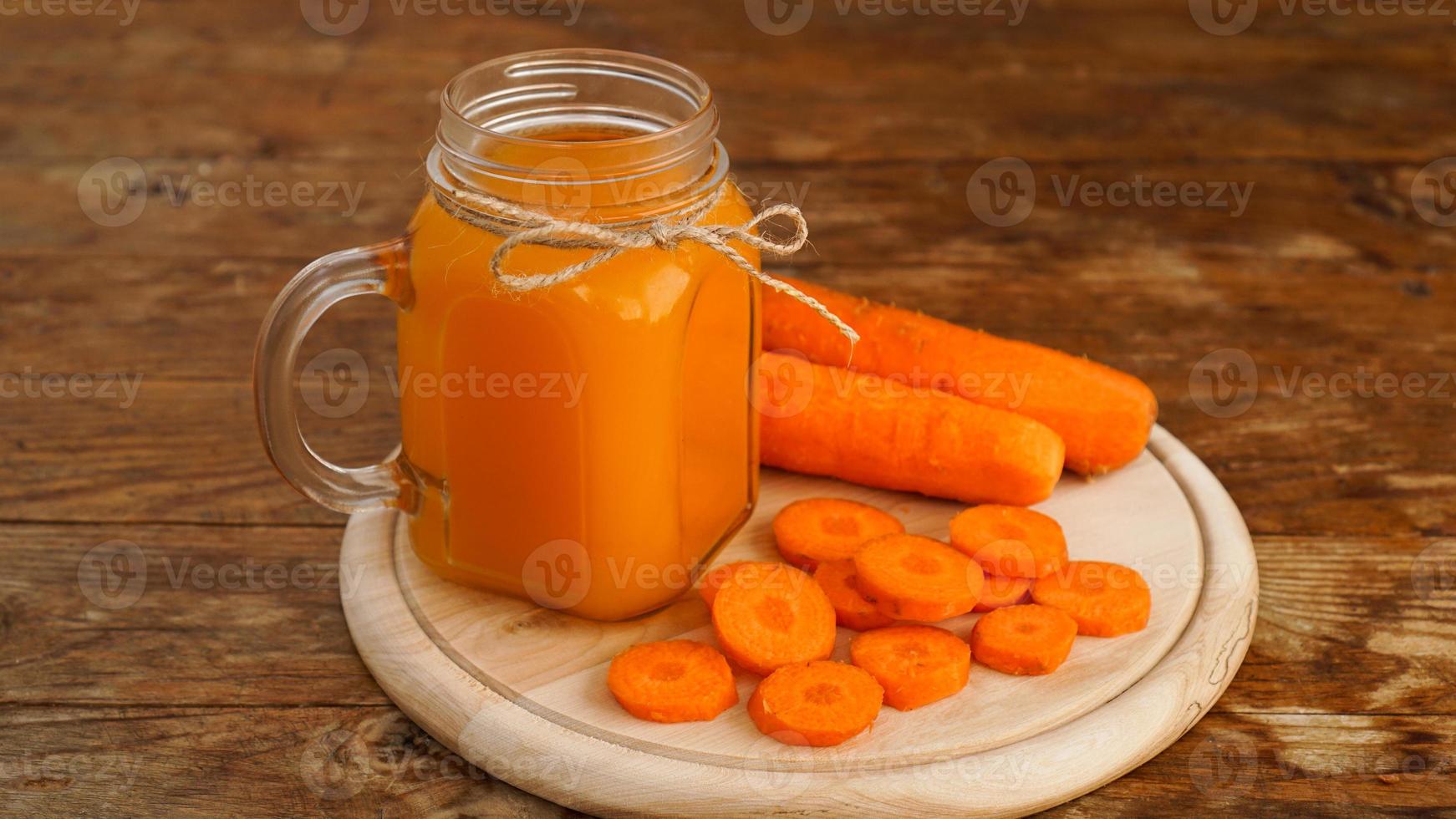 Jugo de zanahoria naranja brillante en un frasco de vidrio sobre un fondo de madera foto