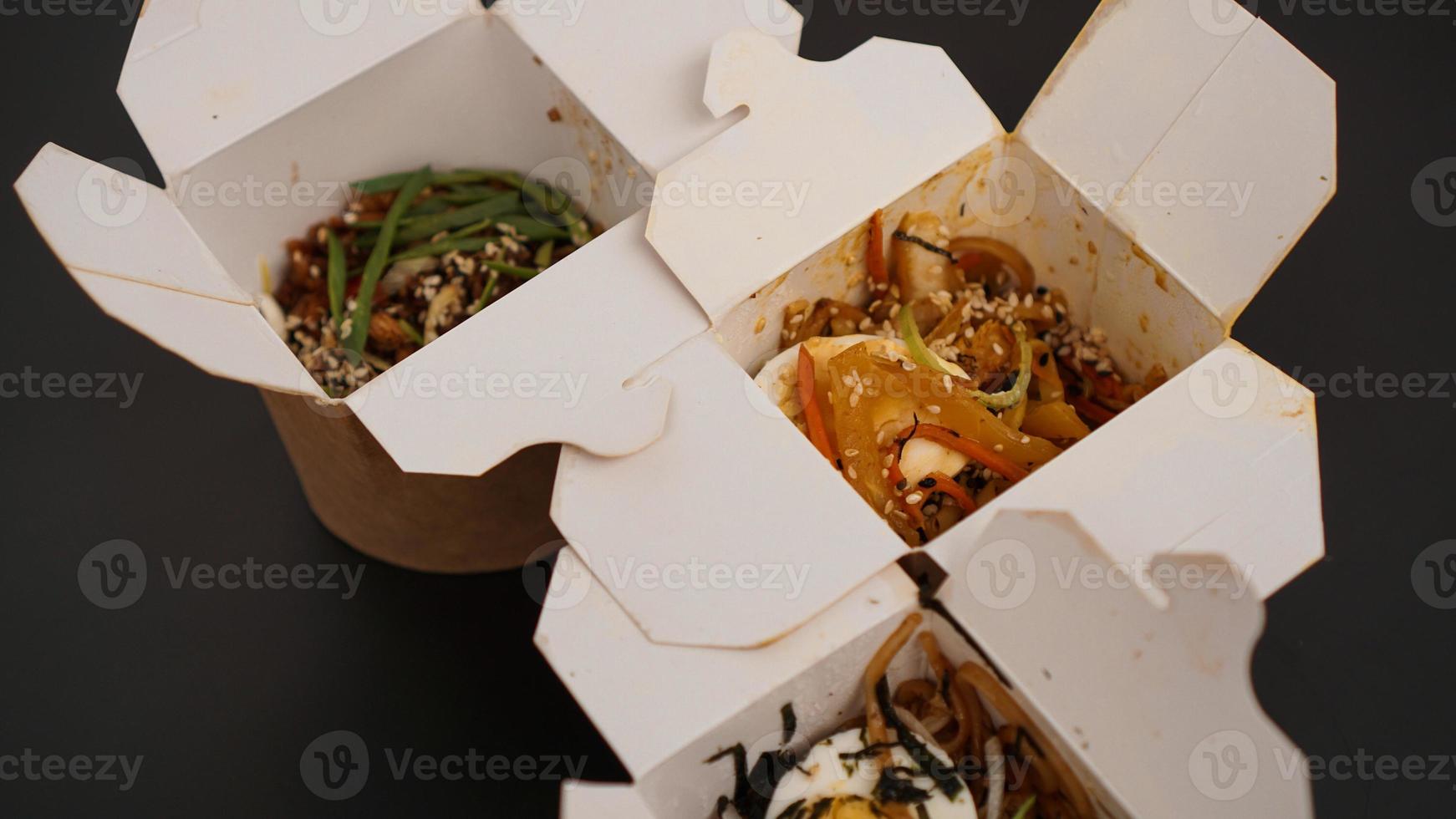 Noodles with pork and vegetables in take-out box on black table photo