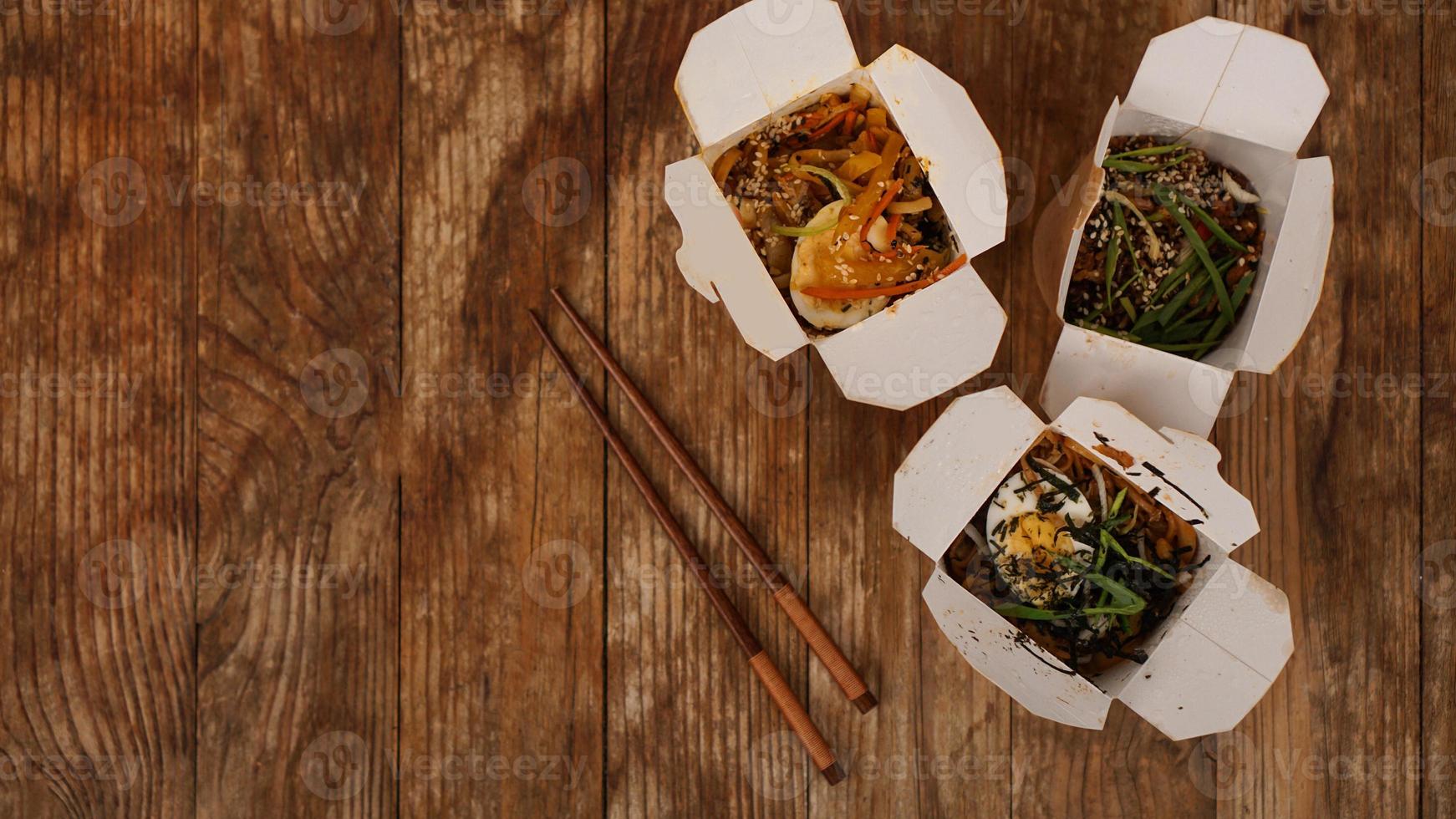 Fideos con carne de cerdo y verduras en caja para llevar sobre mesa de madera foto