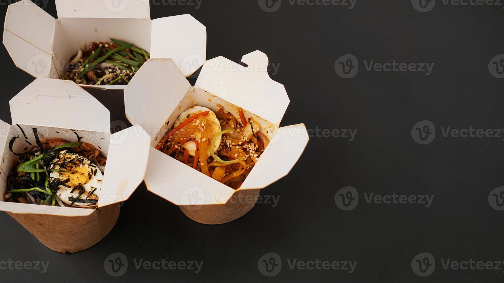 Noodles with pork and vegetables in take-out box on black table photo