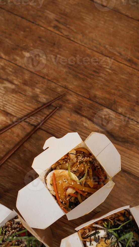 Noodles with pork and vegetables in take-out box on wooden table photo