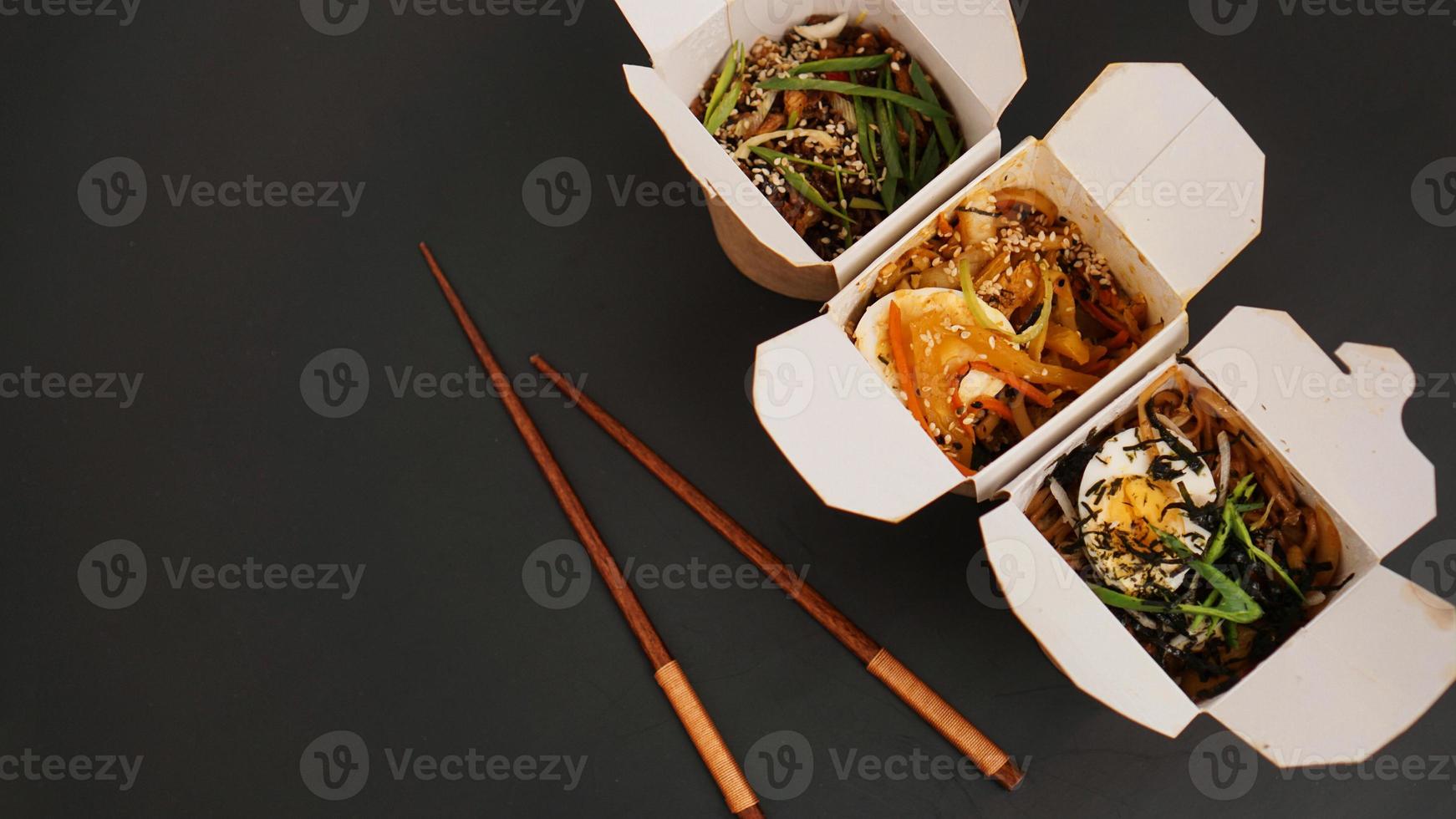 Noodles with pork and vegetables in take-out box on black table photo