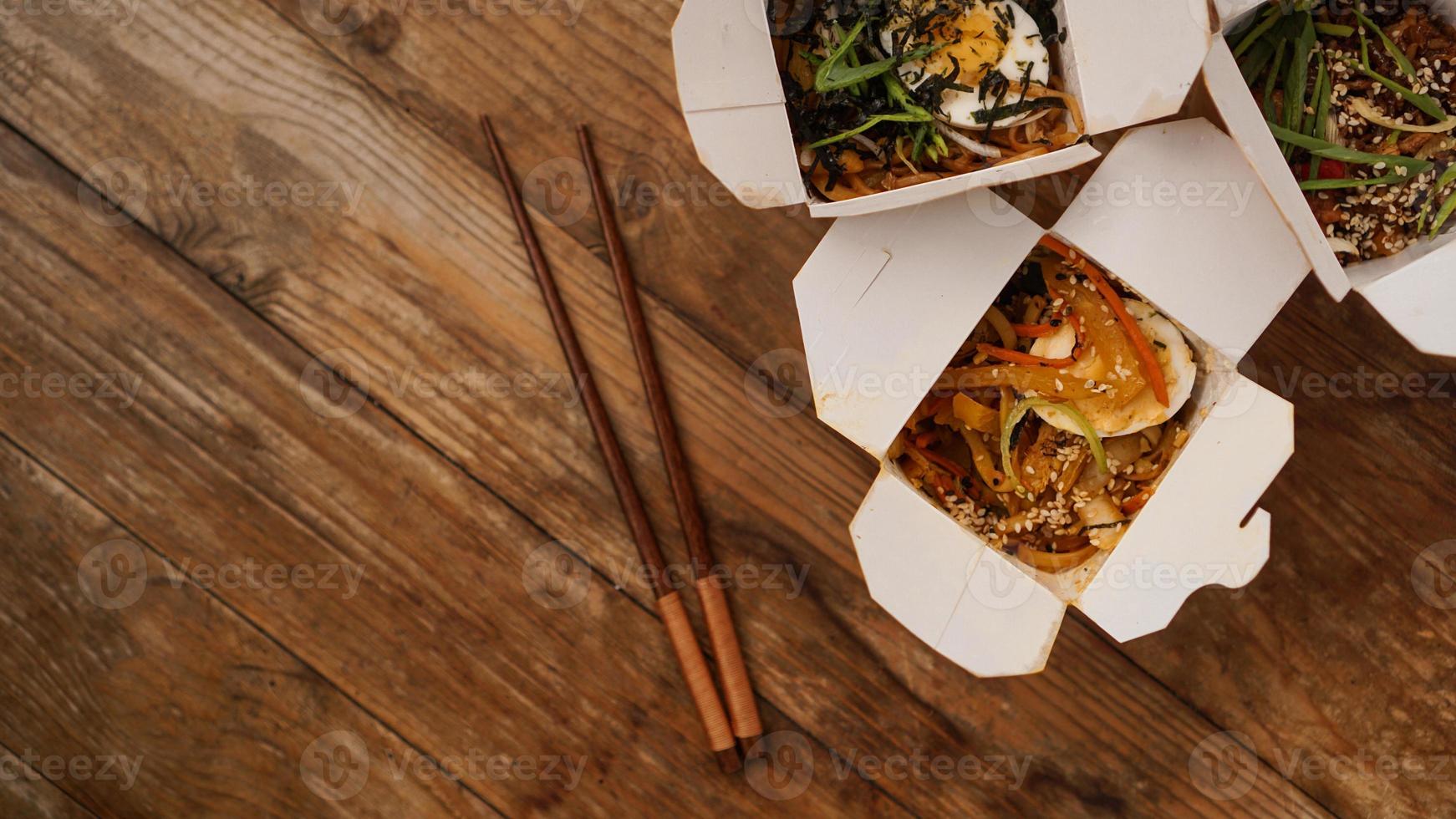 Noodles with pork and vegetables in take-out box on wooden table photo