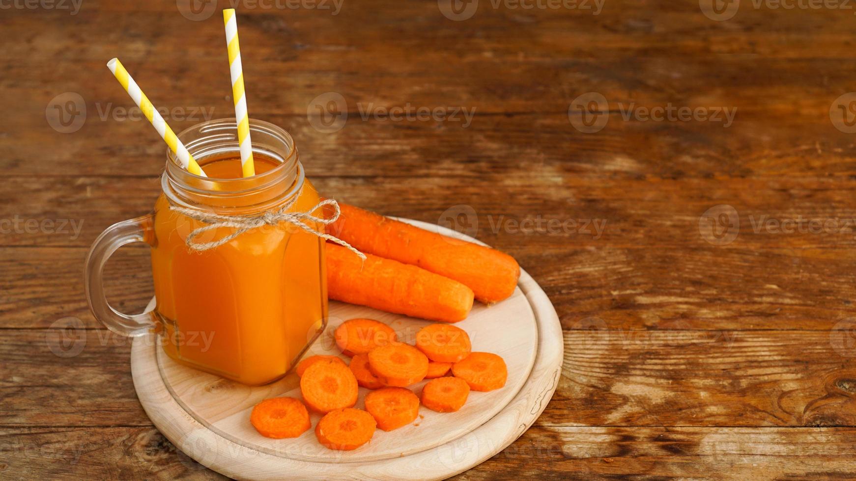 Jugo de zanahoria naranja brillante en un frasco de vidrio sobre un fondo de madera foto