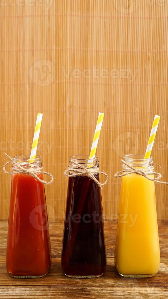 Three multicolored drinks in the bottles on a wooden bamboo background photo