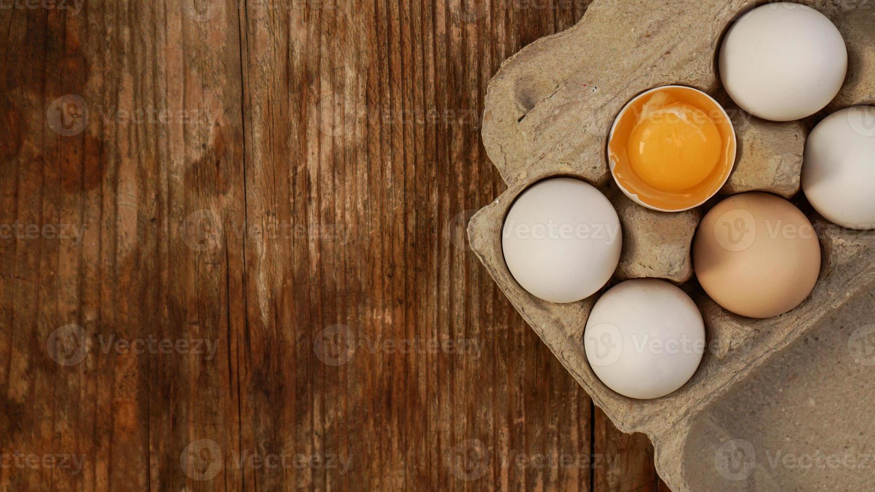 White eggs carton and cracked egg half with yolk top view photo