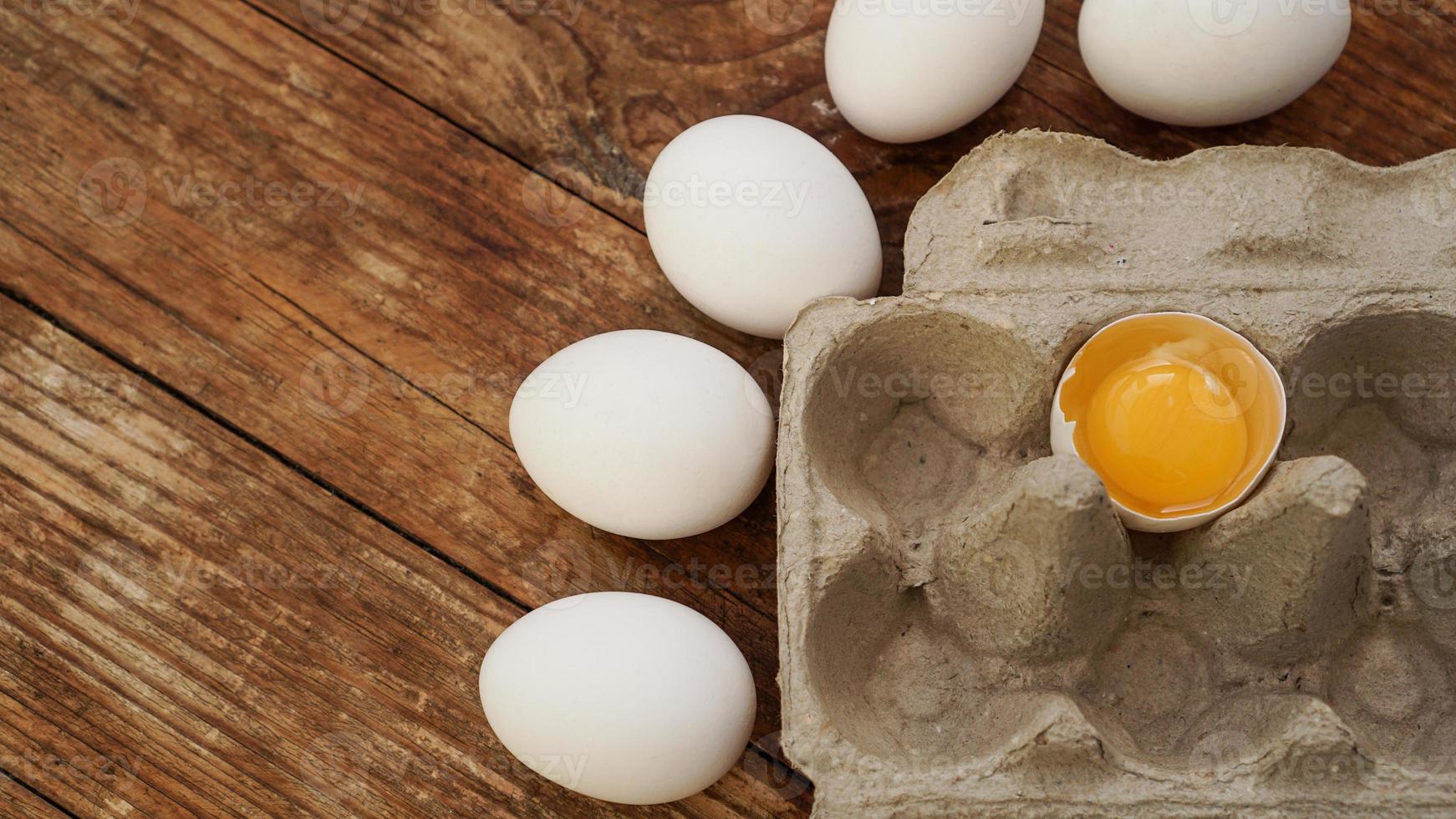 White eggs carton and cracked egg half with yolk top view photo