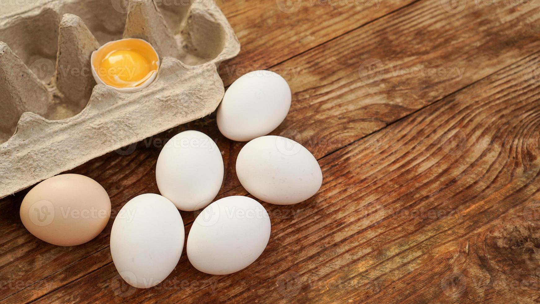 Cartón de huevos blancos y la mitad del huevo agrietado con vista superior de la yema foto