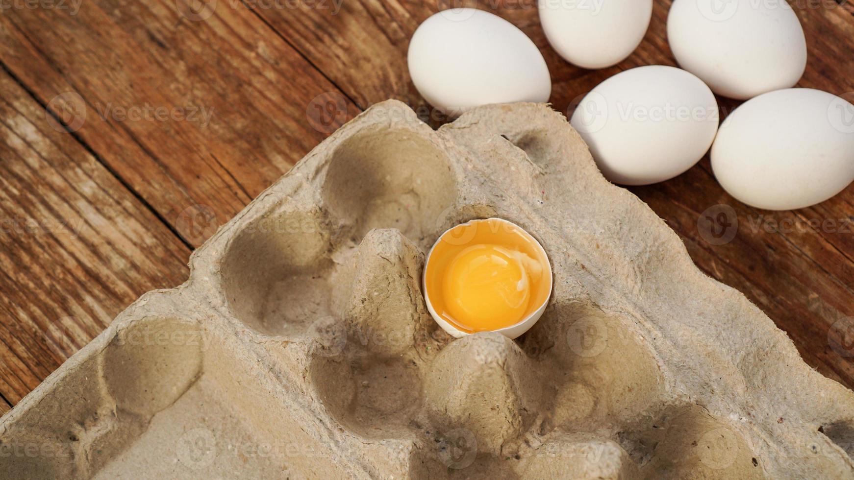 White eggs carton and cracked egg half with yolk top view photo