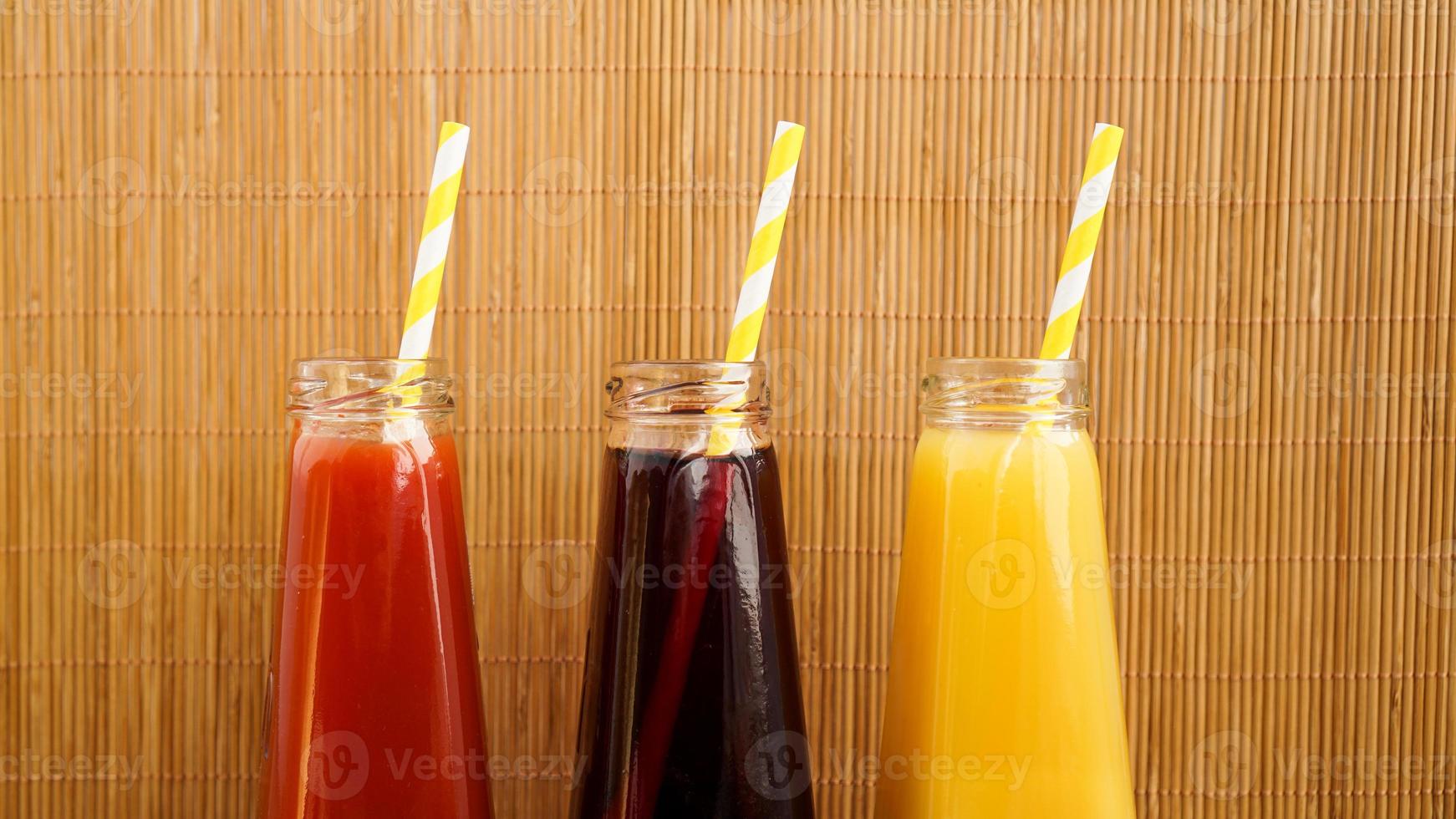 Tres bebidas multicolores en las botellas sobre un fondo de bambú de madera foto