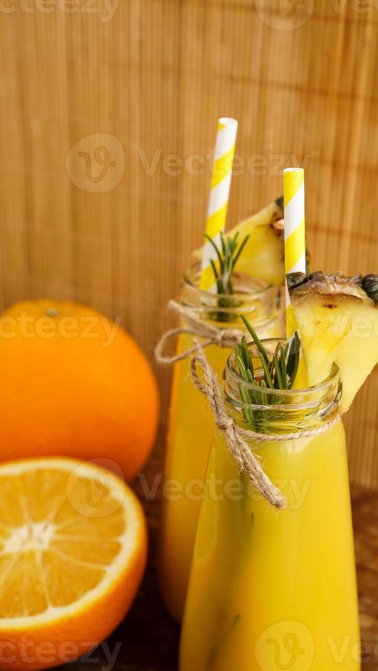 Two bottles of tropical juice with paper straws. Oranges and pineapple photo