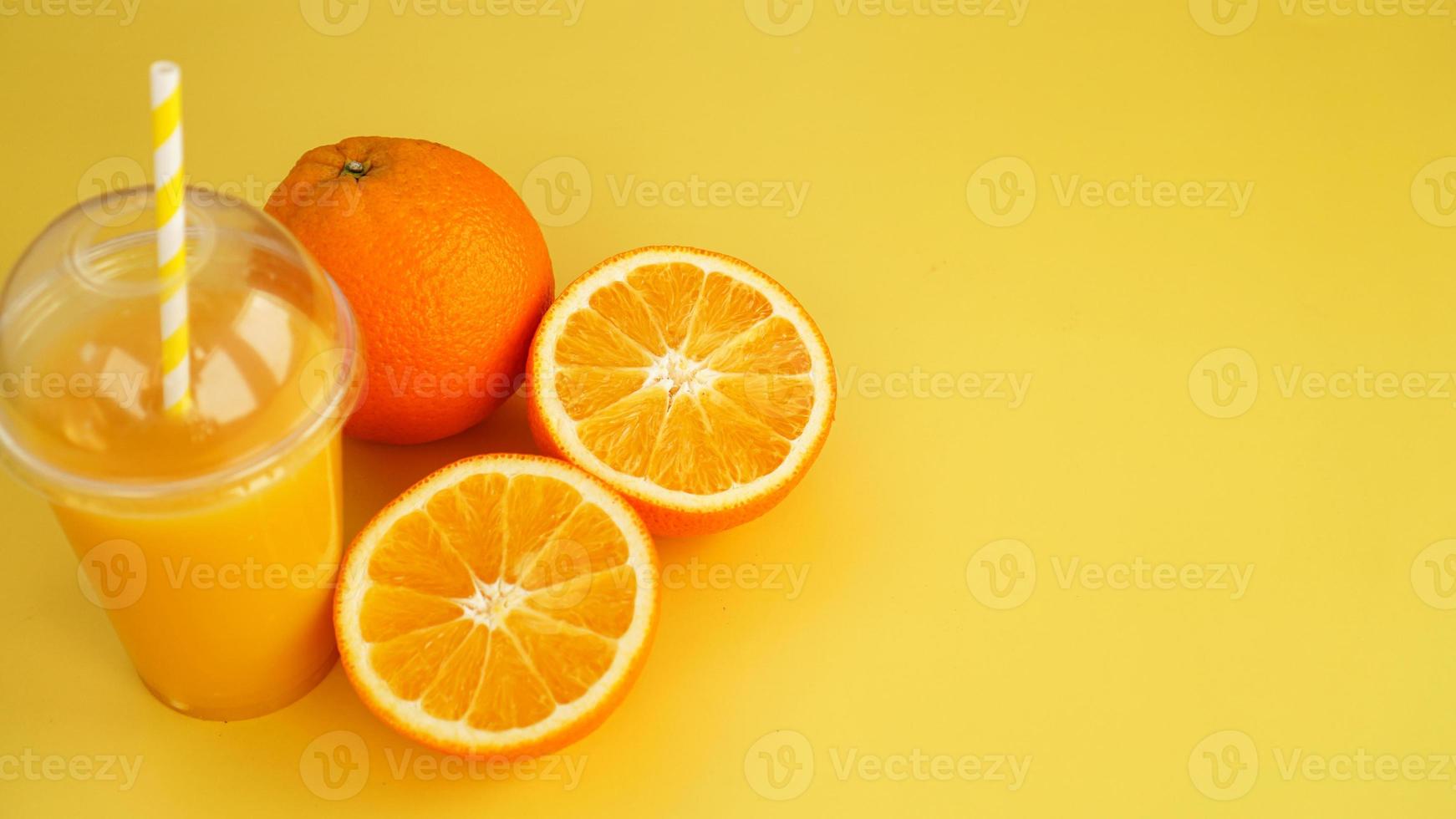 jugo de naranja en un vaso de plástico con una pajita. naranja en rodajas foto