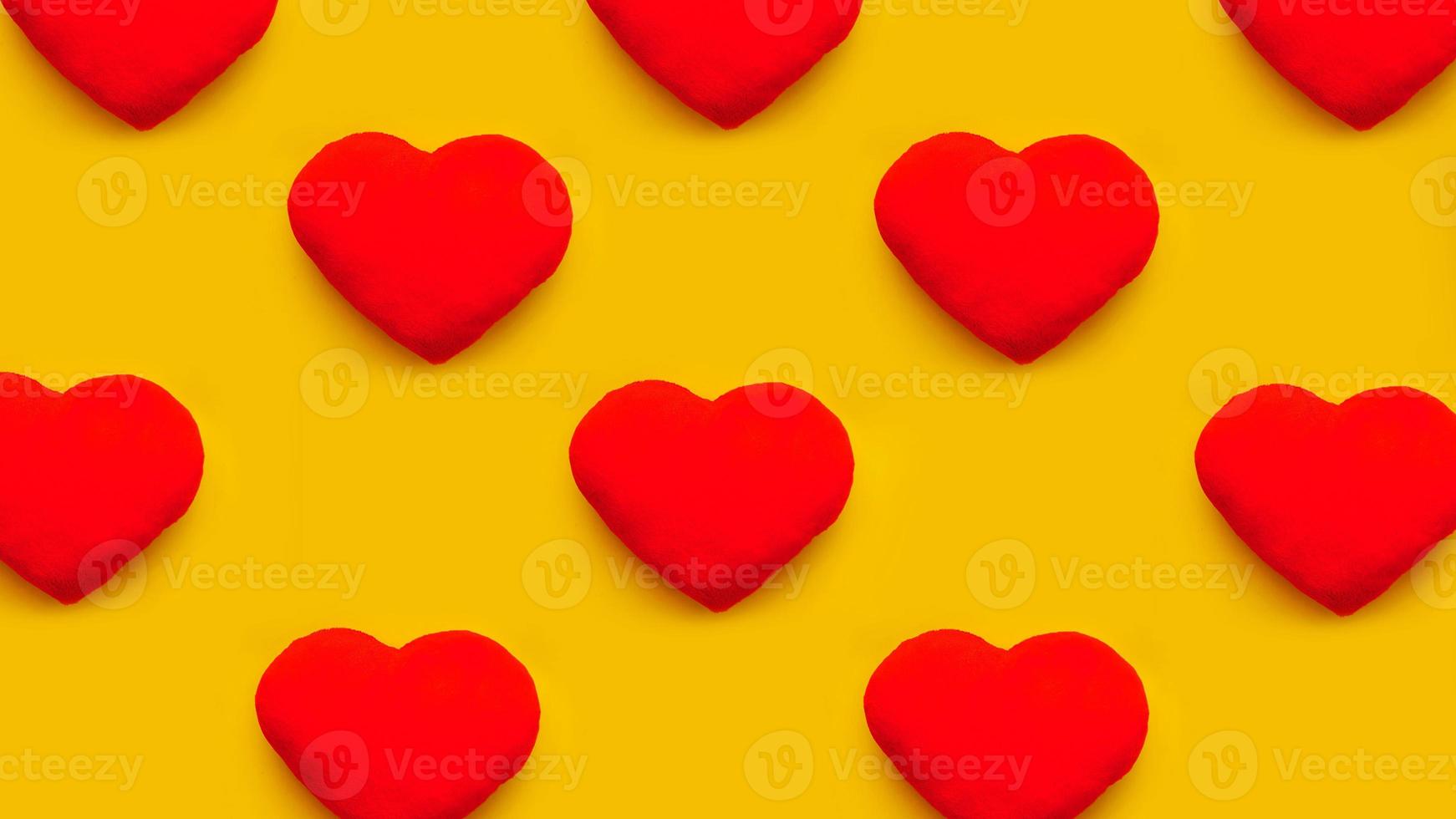 Rows of red heart toys on yellow background. Flat lay photo