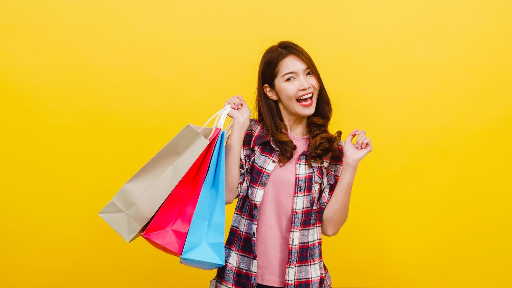 Happy young Asian lady carrying shopping bags with hand raising up. photo