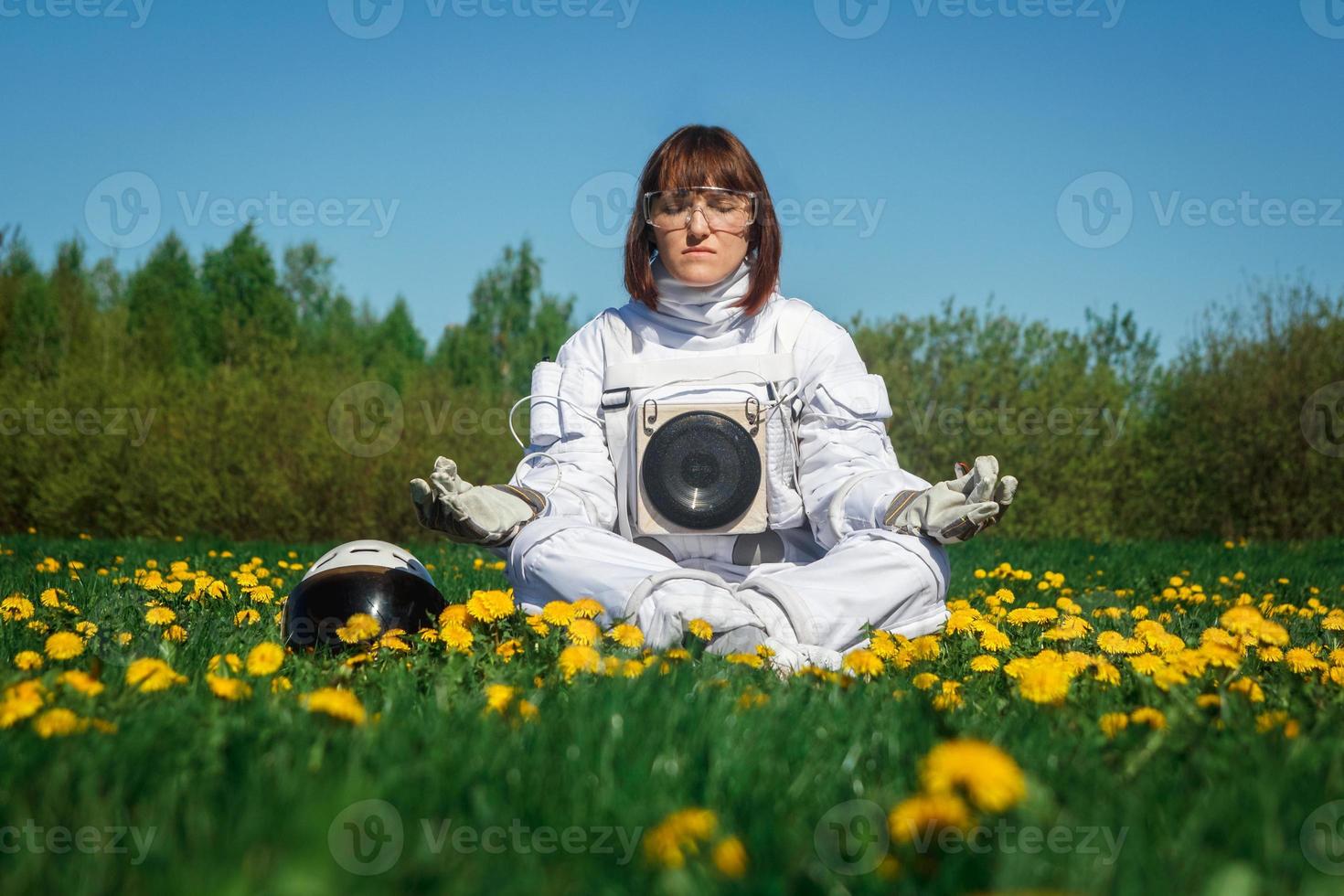 Woman astronaut sits on a green lawn in a meditative position photo