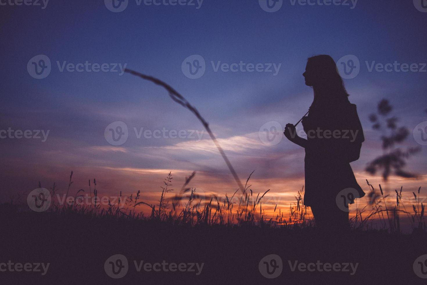 Silhouette of girl with a backpack at a meadow on background of sunset photo