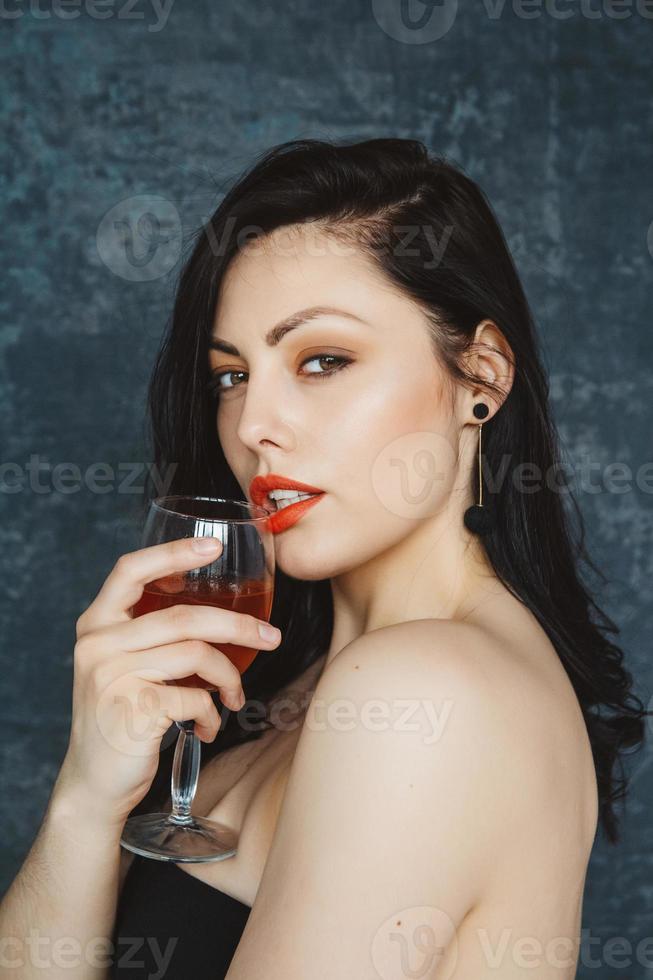 Hermosa mujer joven con copa de vino sobre fondo gris foto