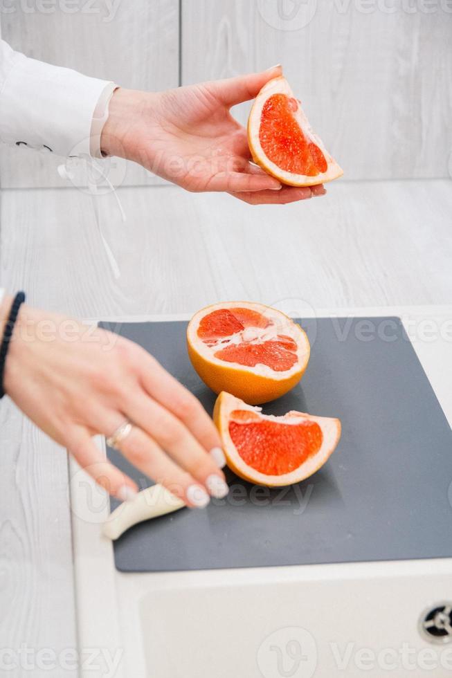 Woman's hands cutting fresh grapefruit on kitchenr photo