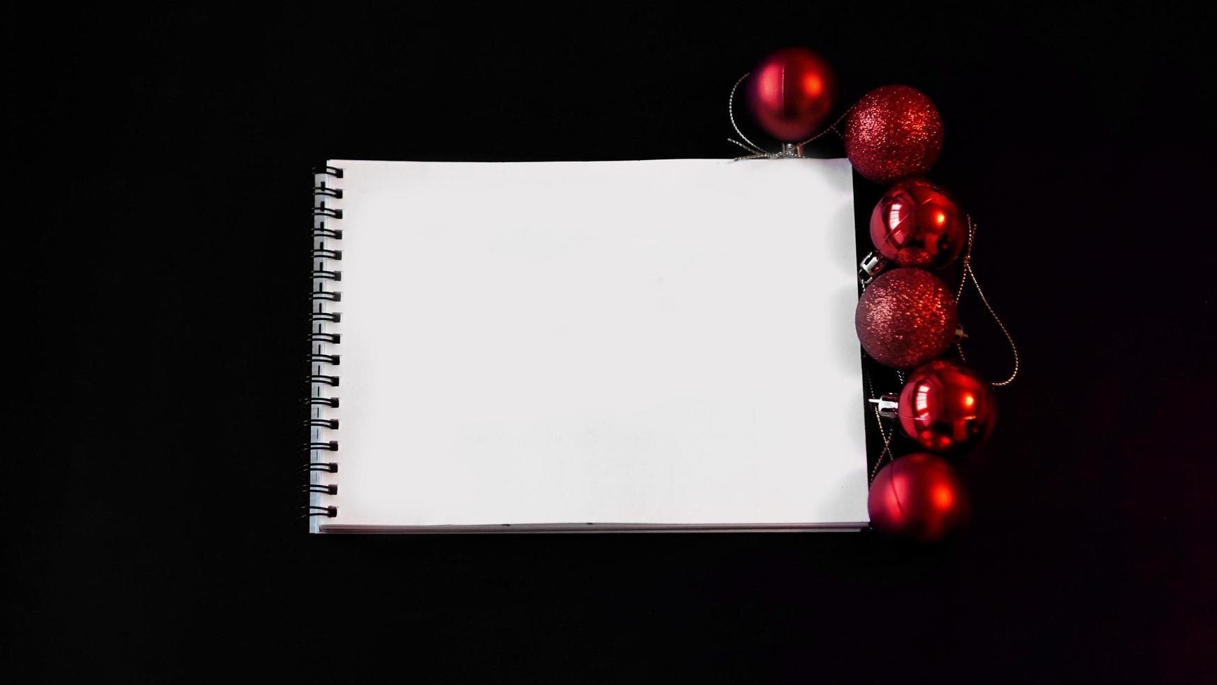 Open blank notebook, Christmas balls on black background photo