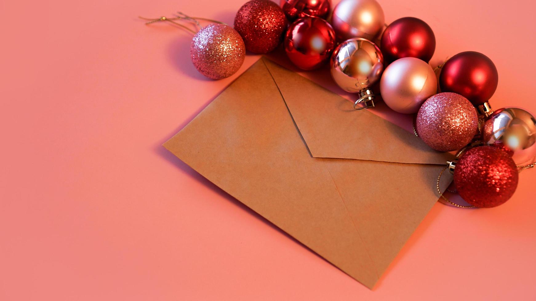 sobre de papel artesanal con bolas navideñas rojas y rosas sobre rosa foto