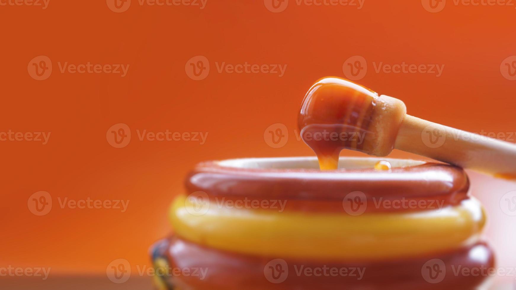 Honey dripping from honey dipper on yellow background photo