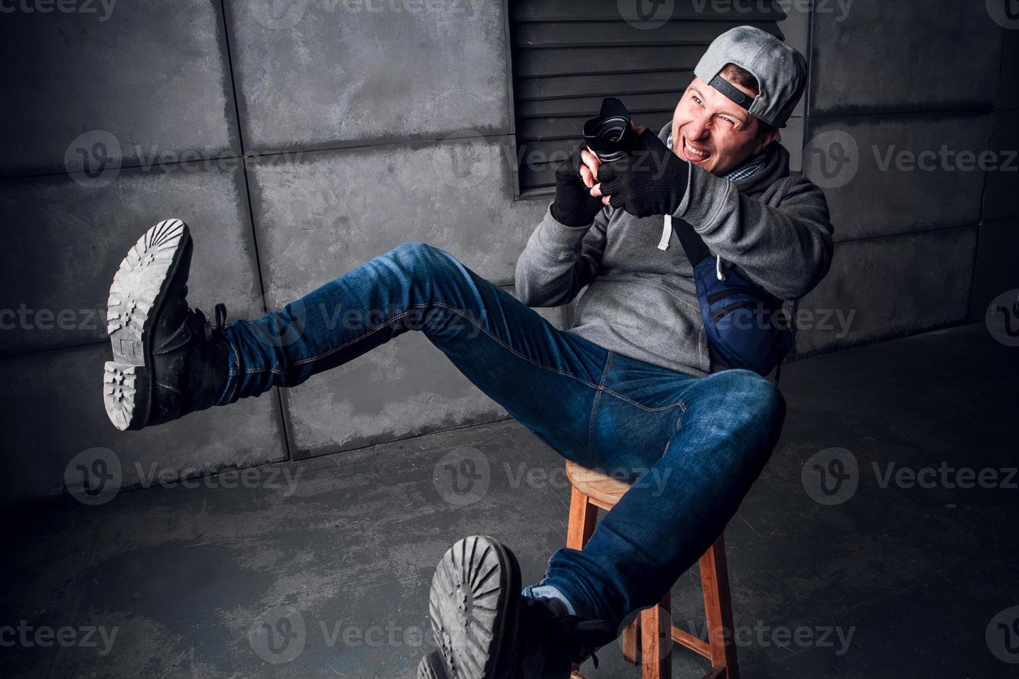 Man with a camera and a funny face sitting on a chair in a gray studio photo