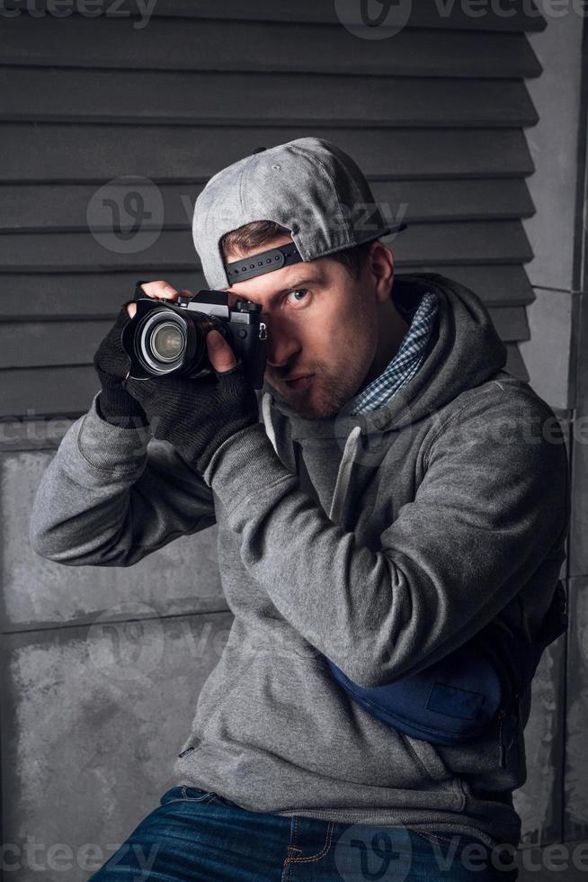 Man with a camera and a funny face sitting on a chair in a gray studio photo