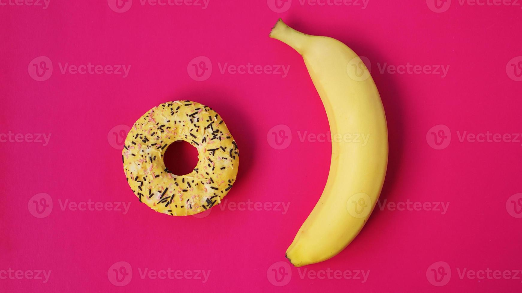 Yellow banana and donut on pink background. Above view photo