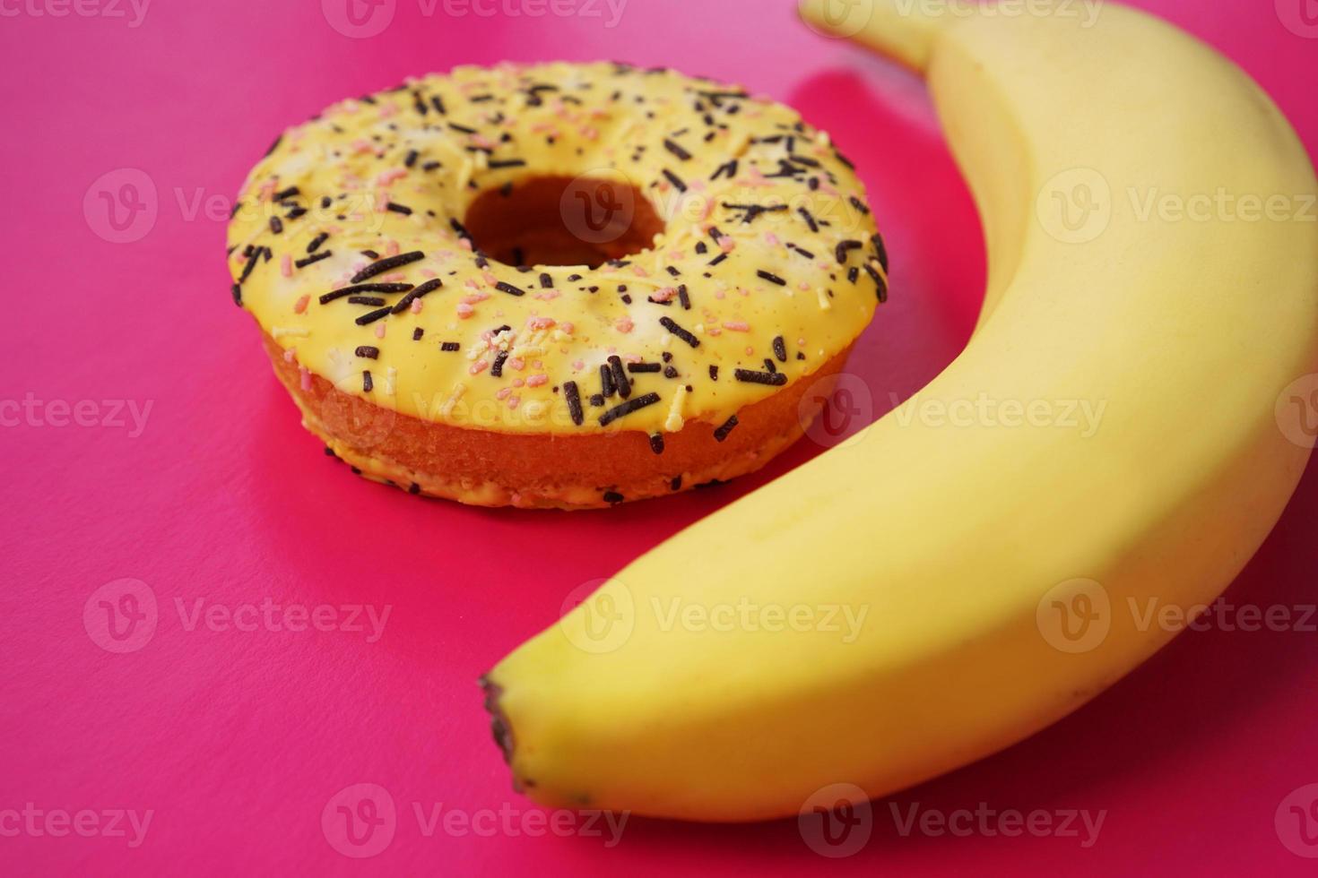 Yellow banana and donut on pink background. Above view photo