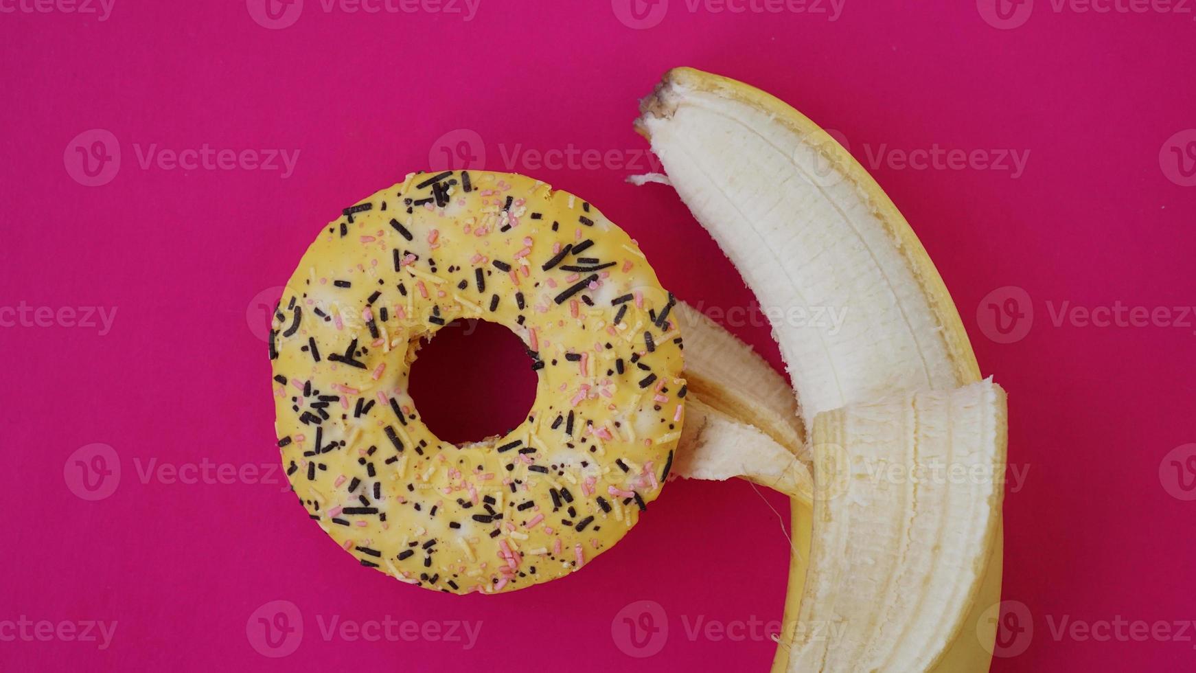 Donut dulce y plátano sobre fondo de color rosa foto