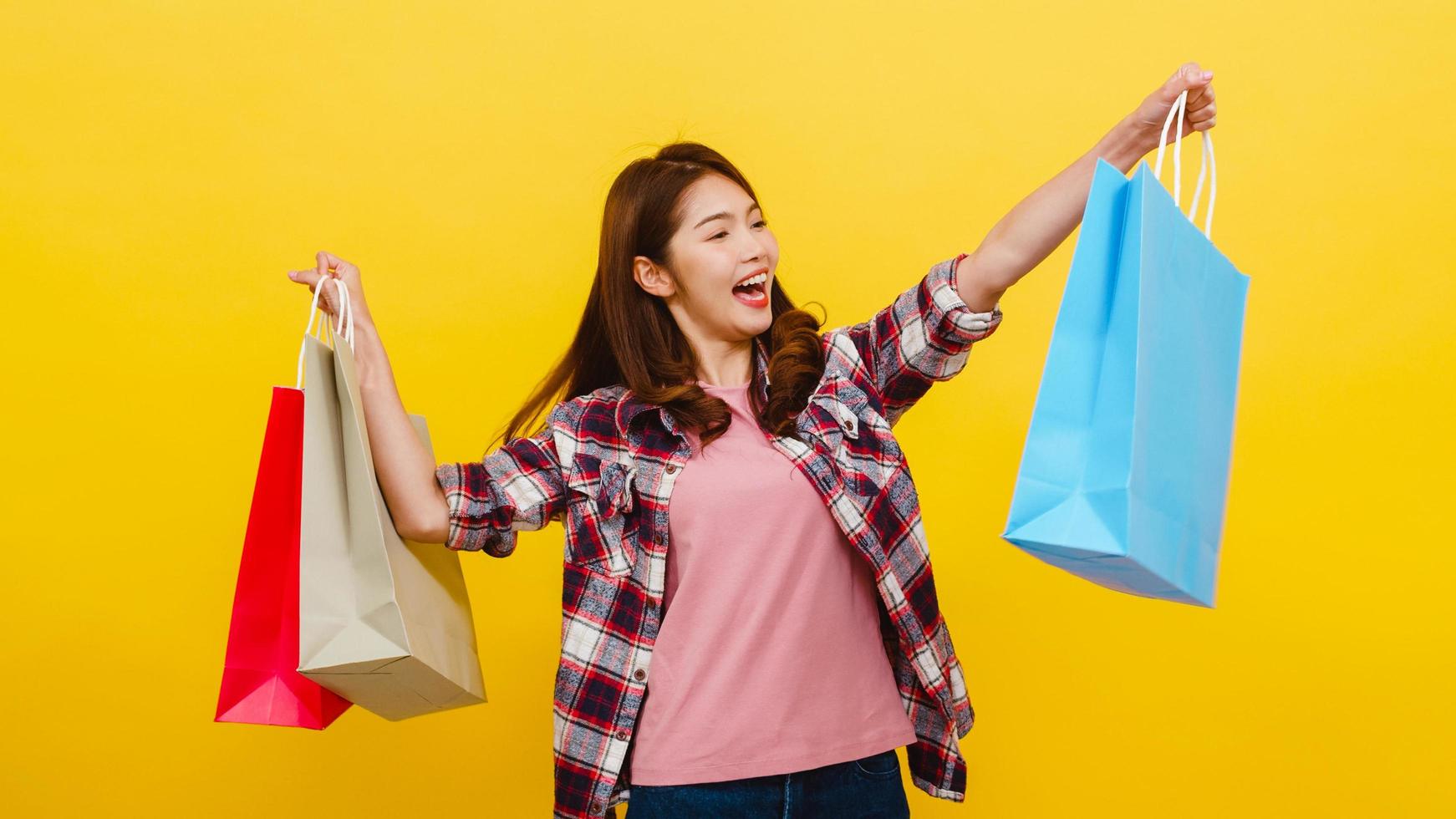 Happy young Asian lady carrying shopping bags with hand raising up. photo