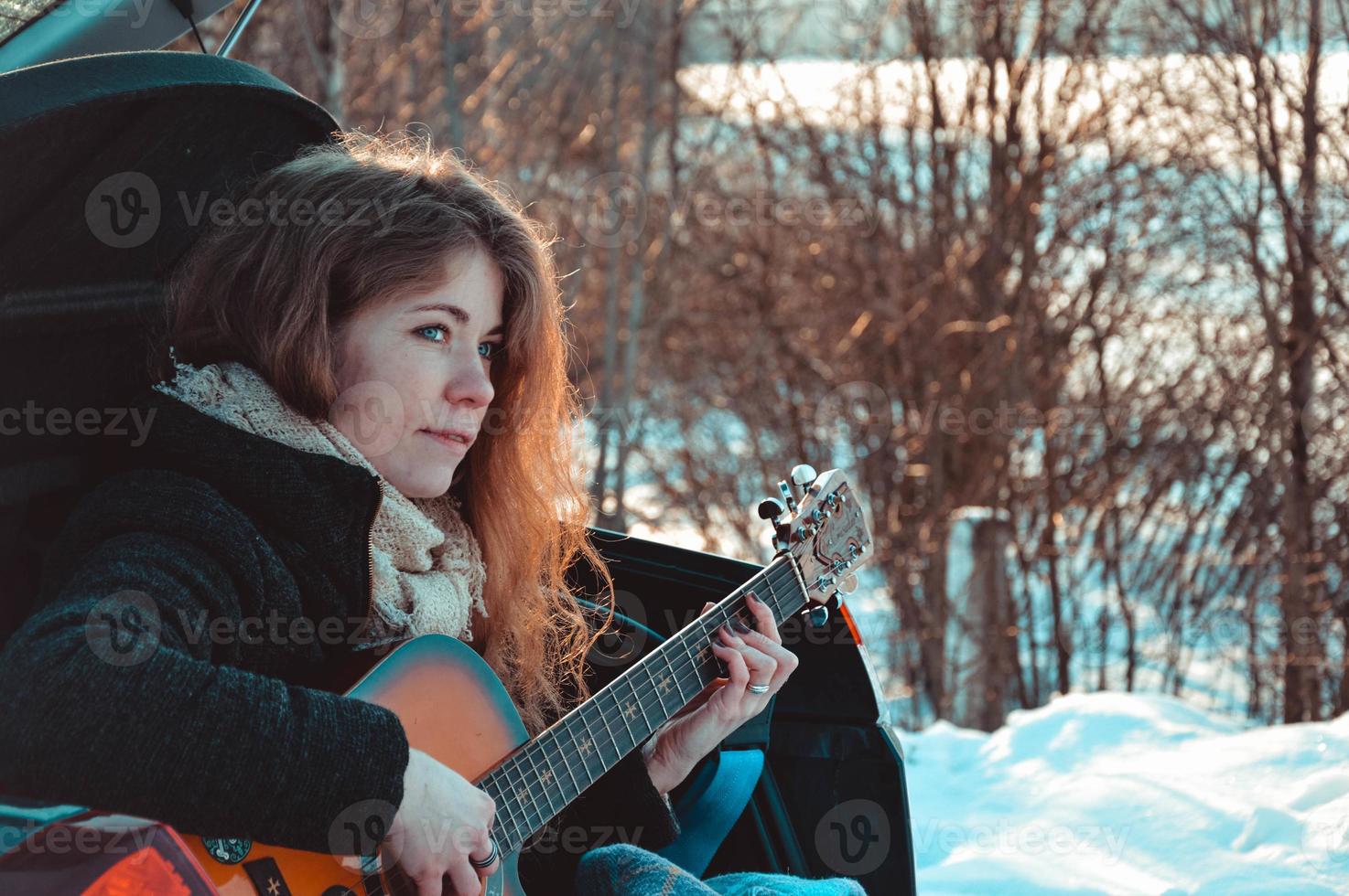 Woman tourist sitting on car and playing guitar photo