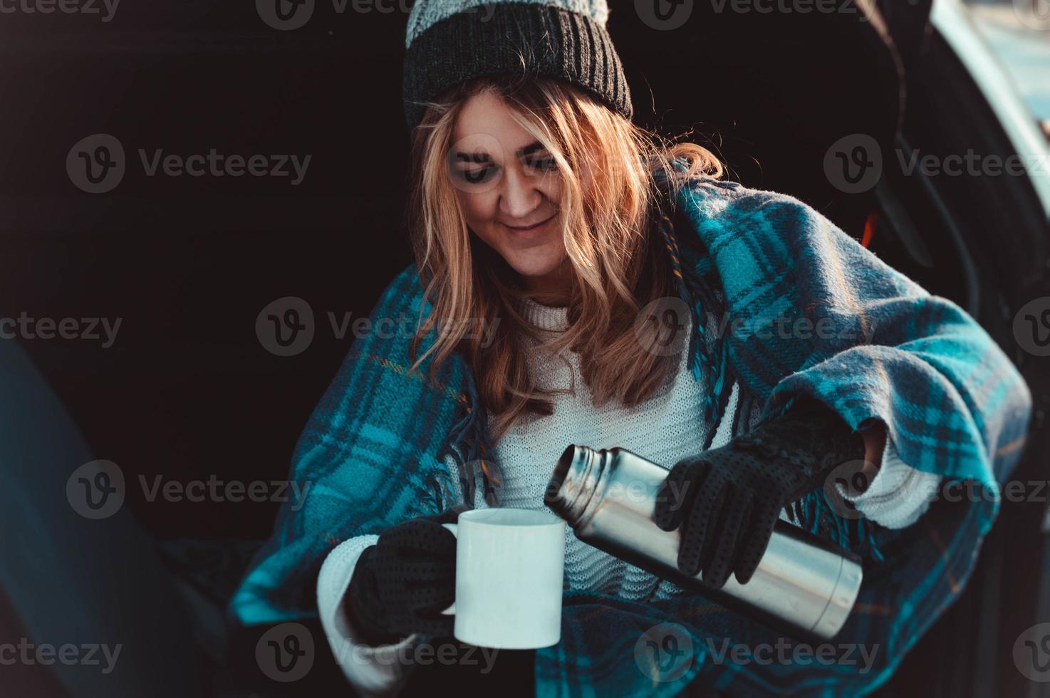 Mujer joven sentada en el maletero del coche con taza de café foto
