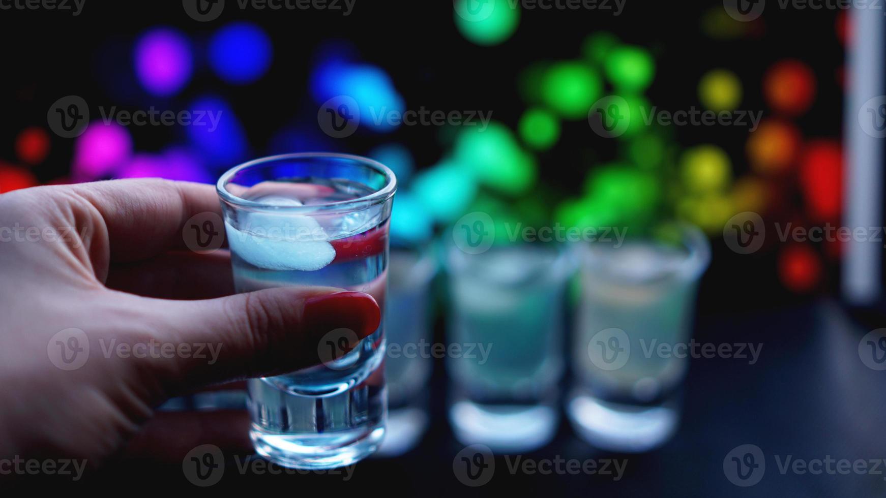 Mano femenina con un trago de alcohol, neón fondo borroso foto