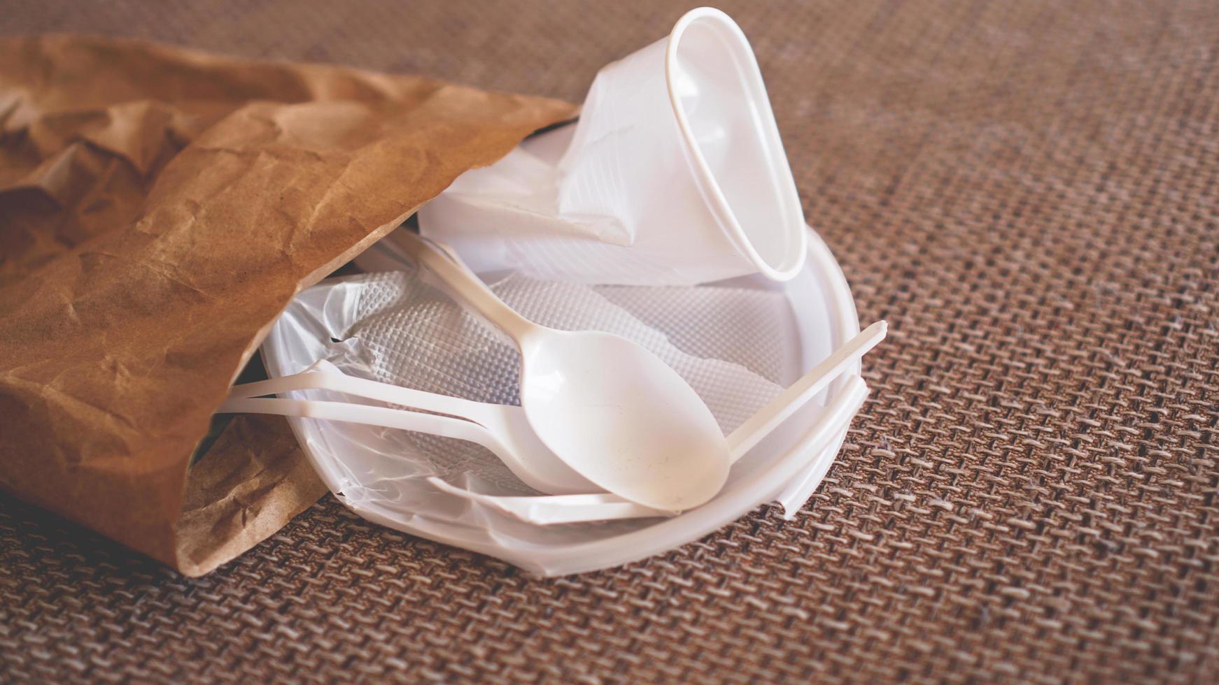 White crumpled plastic dishes in a paper packet on beige background photo