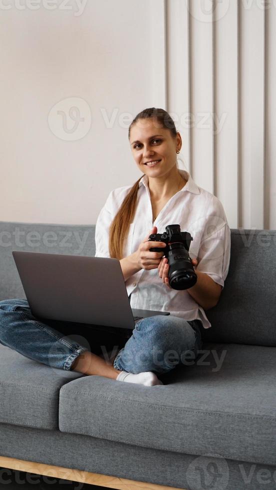 Mujer joven feliz con cámara de fotos usando el portátil en casa