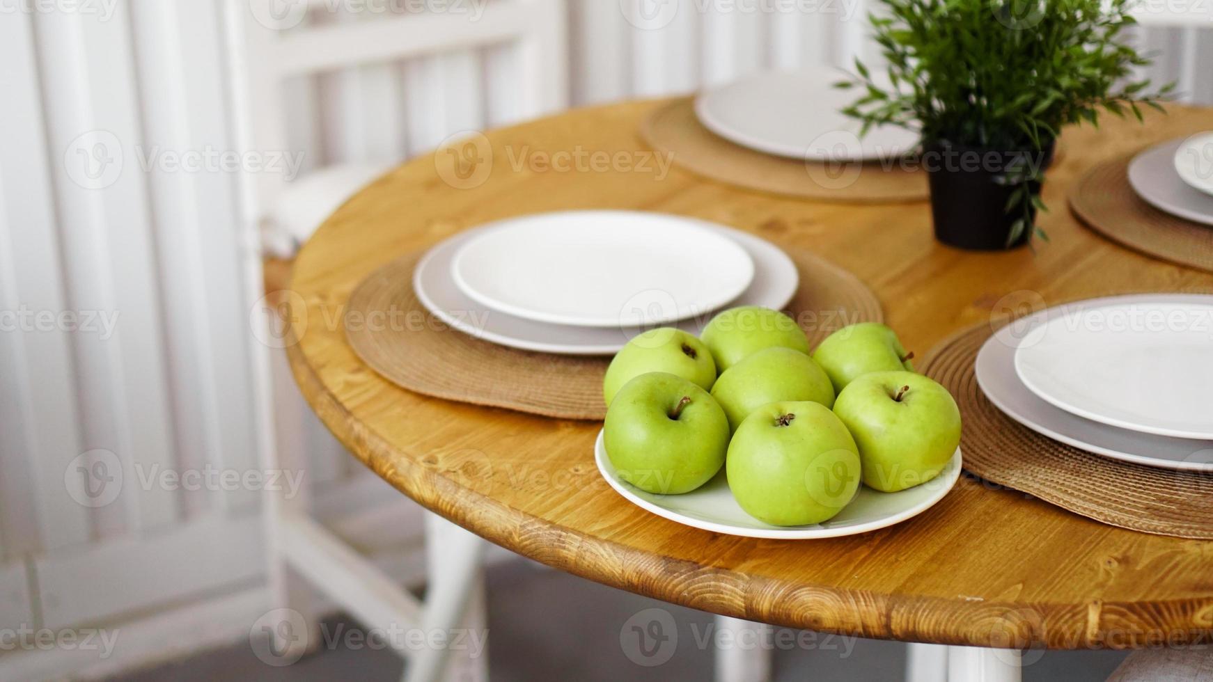 Green apples on a white plate on a wooden table photo