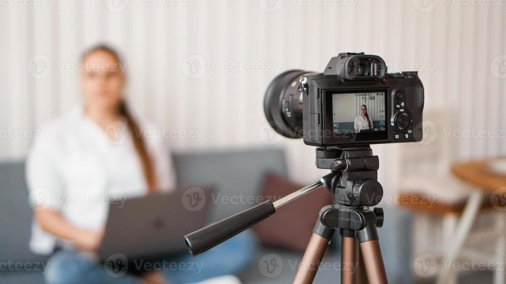 Blogger recording video indoors, selective focus on camera display photo