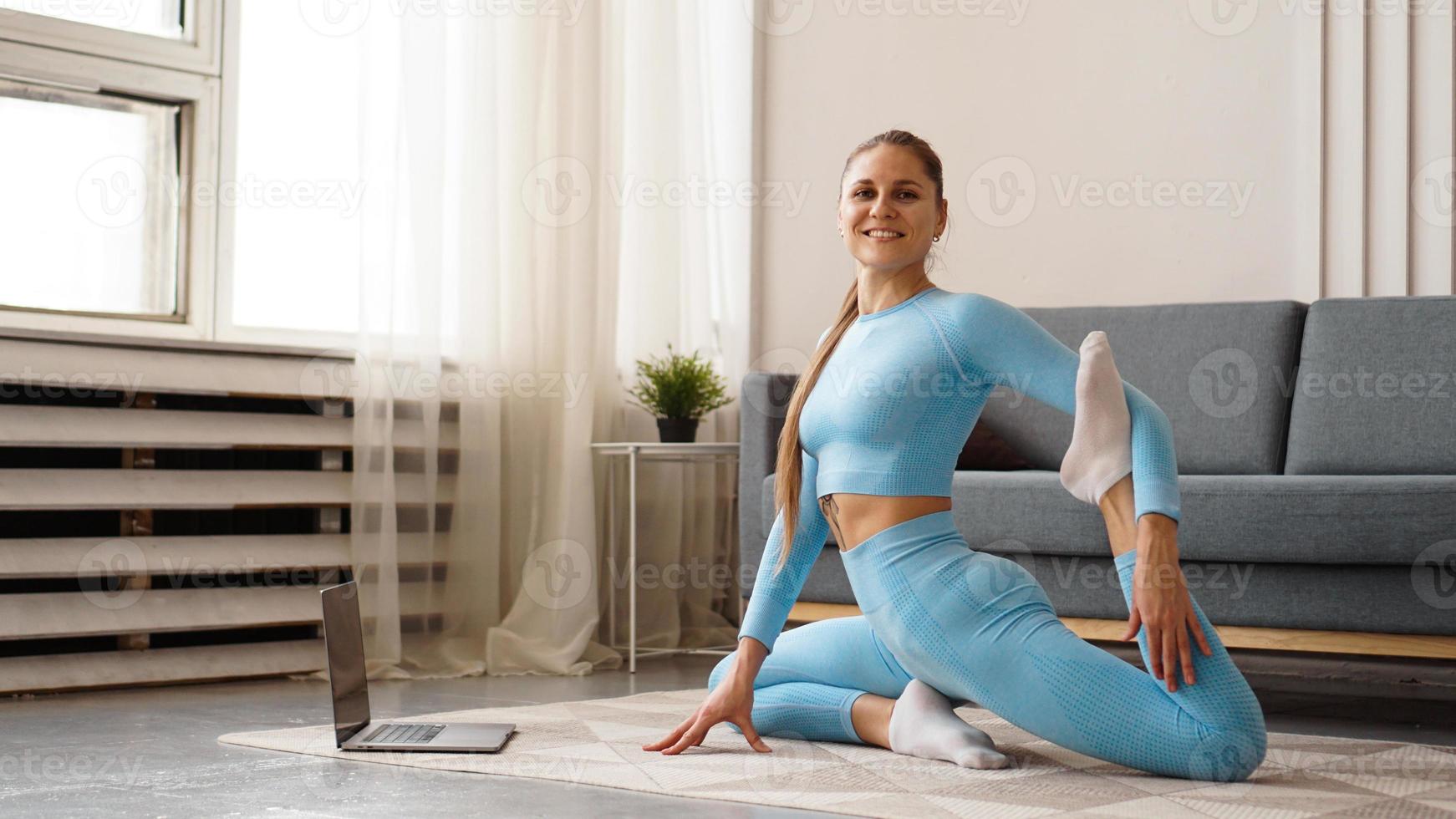 Hermosa joven haciendo ejercicio físico en casa con su computadora portátil foto