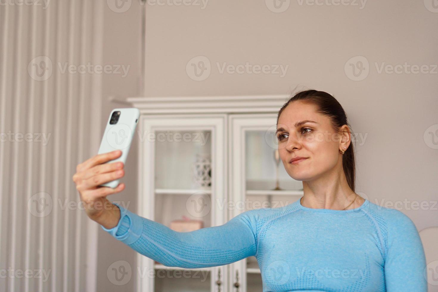 Indoor shot of beautiful woman wearing sports clothes, taking selfie photo