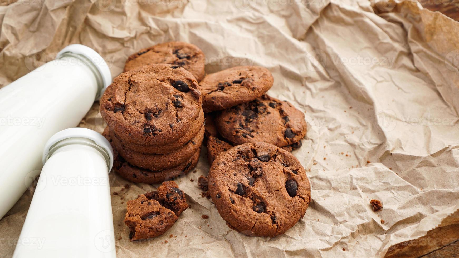 galletas con gotas de chocolate sobre papel artesanal y botellas de leche foto