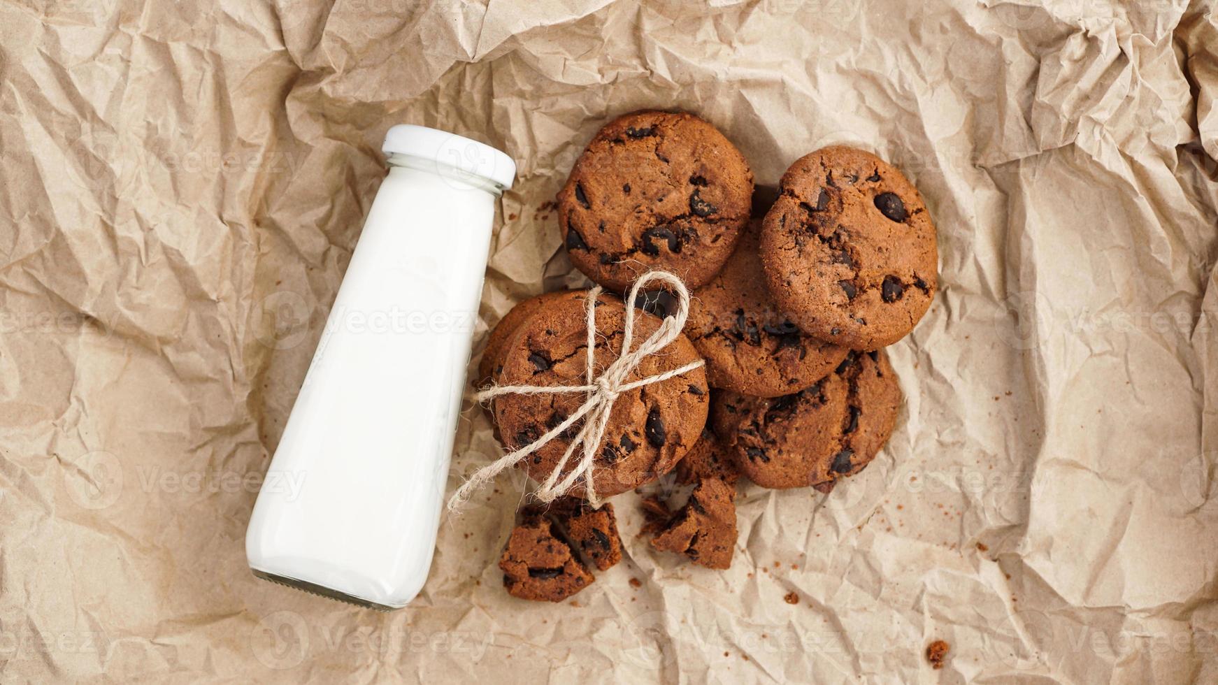 galletas con gotas de chocolate sobre papel artesanal y botella de leche foto