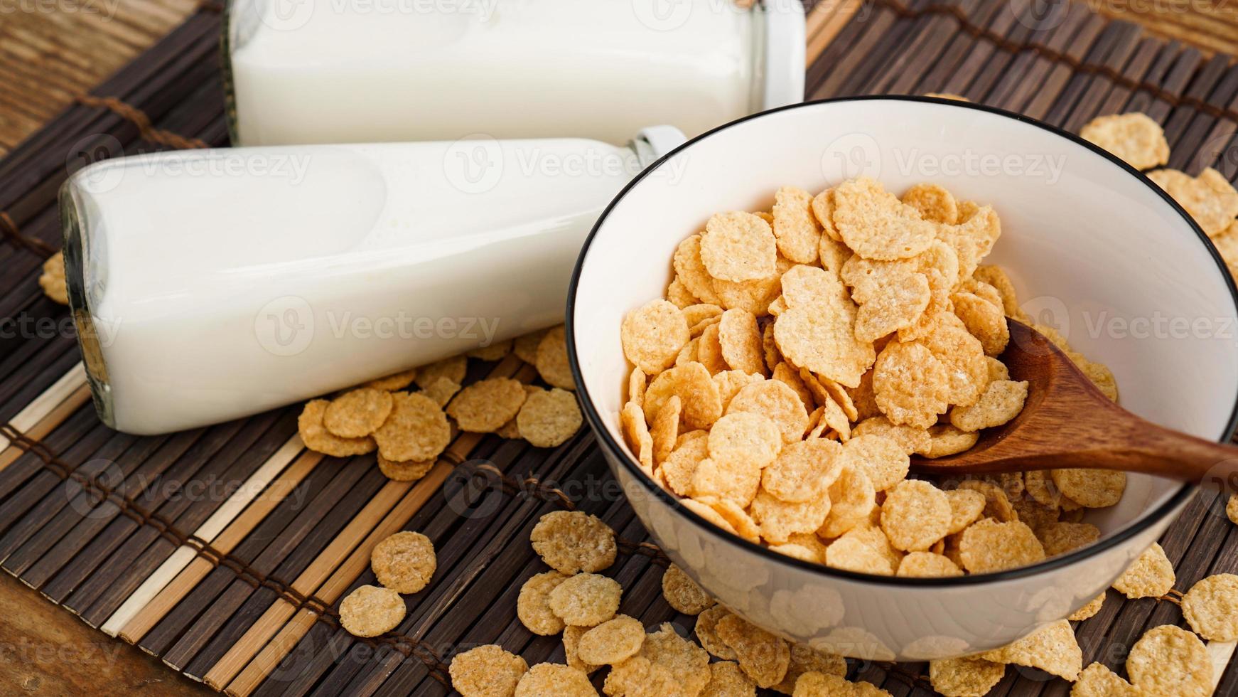 Healthy cornflakes and milk and a wooden spoon on a bamboo napkin. photo