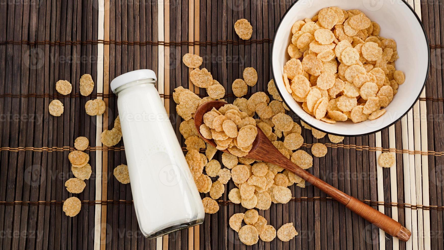 Healthy cornflakes and milk and a wooden spoon on a bamboo napkin. photo